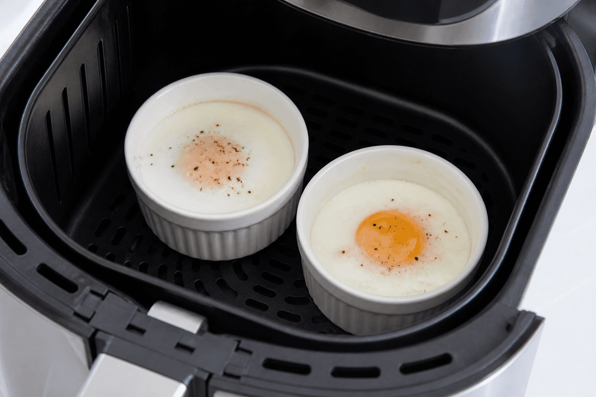 Poached eggs cooking in ramekins in the air fryer basket