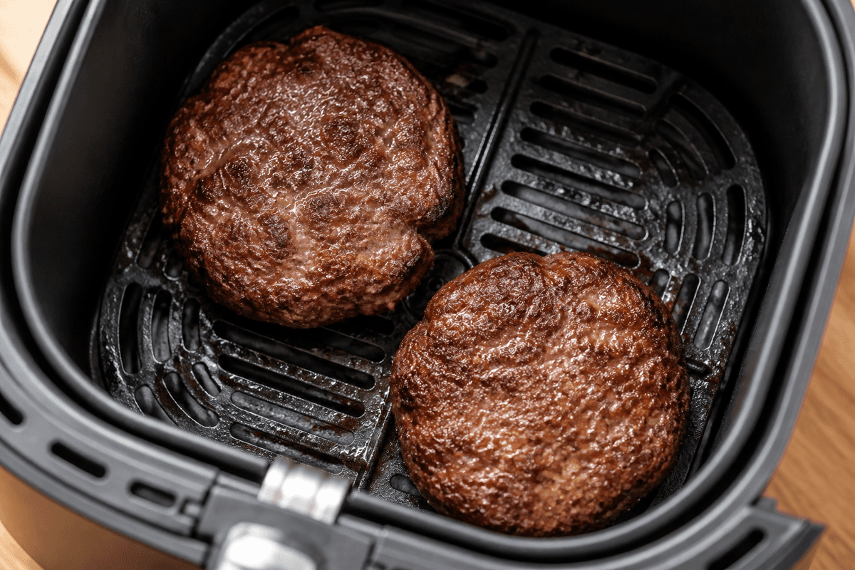 Burger patties cooking in the air fryer basket