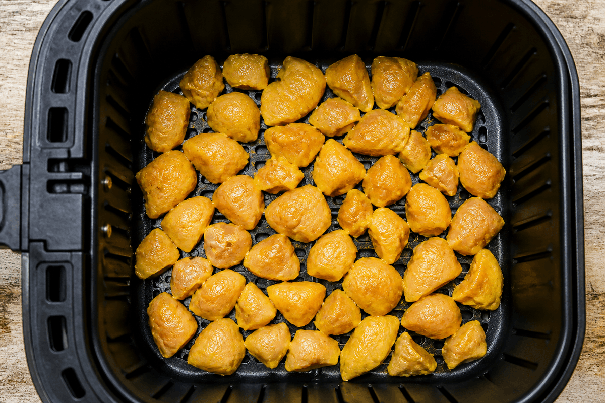 Irregular-cut marinated chicken pieces in air fryer basket